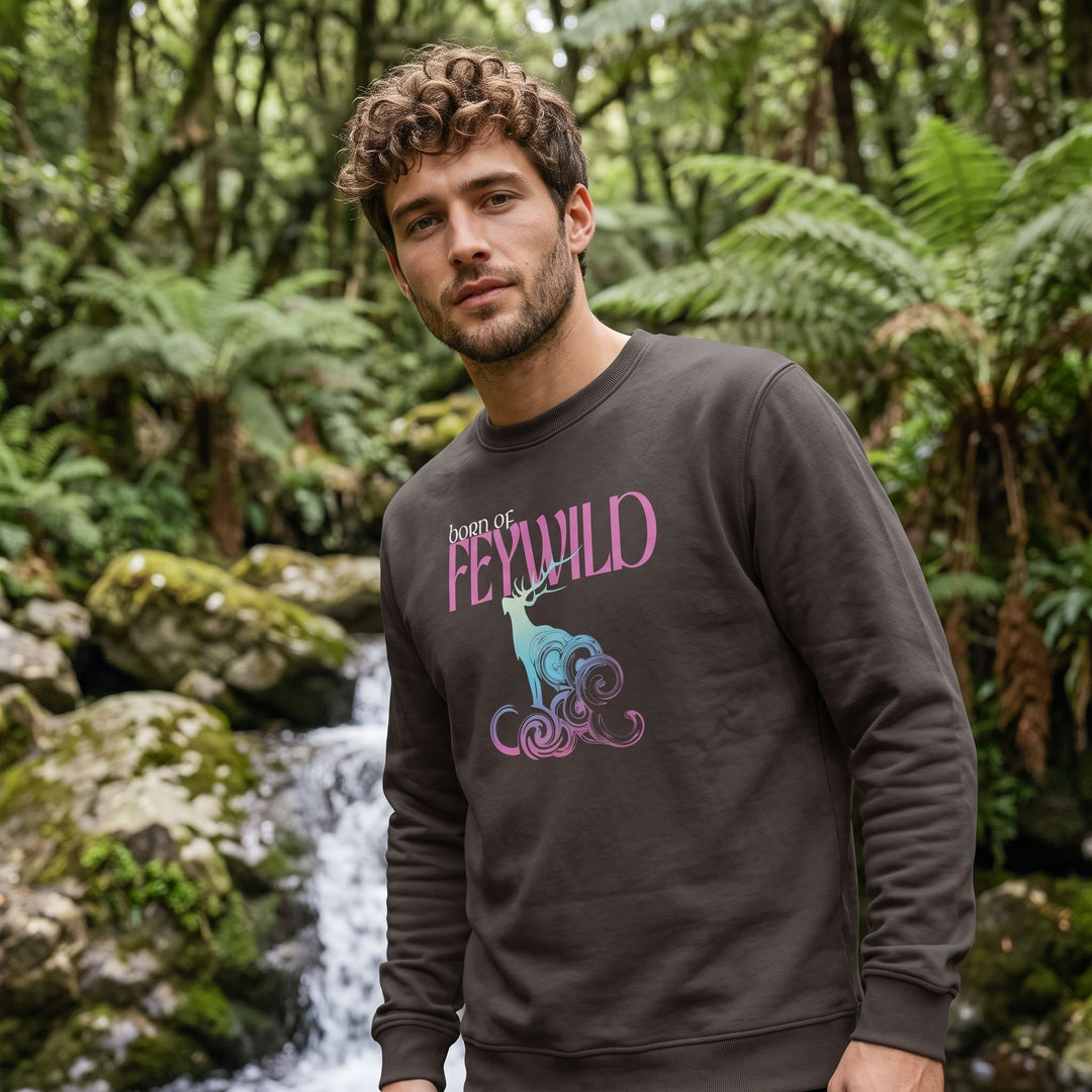 Outdoor scene with a model wearing the Born of Feywild organic sweatshirt featuring a neon-pastel elk stag design, surrounded by greenery under natural daylight.