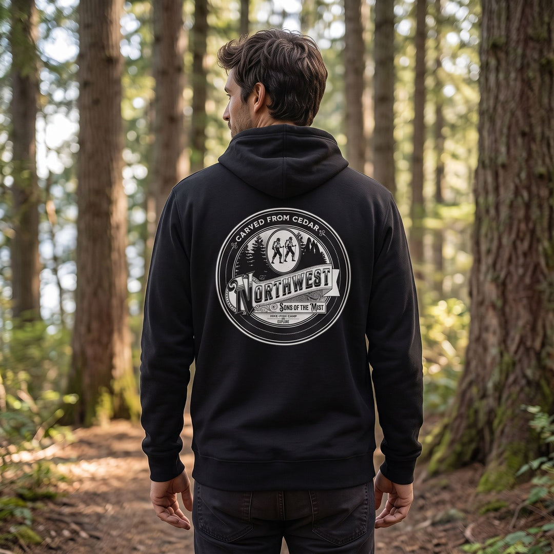 Male model wearing Carved from Cedar Hoodie on a forest trail with blurred greenery, highlighting the nature-inspired eco-friendly outdoor apparel.