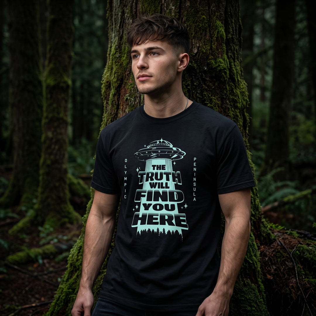 Young adult model wearing UFO-inspired tee with deep blue and dark woods background, captured in dramatic low-key lighting.