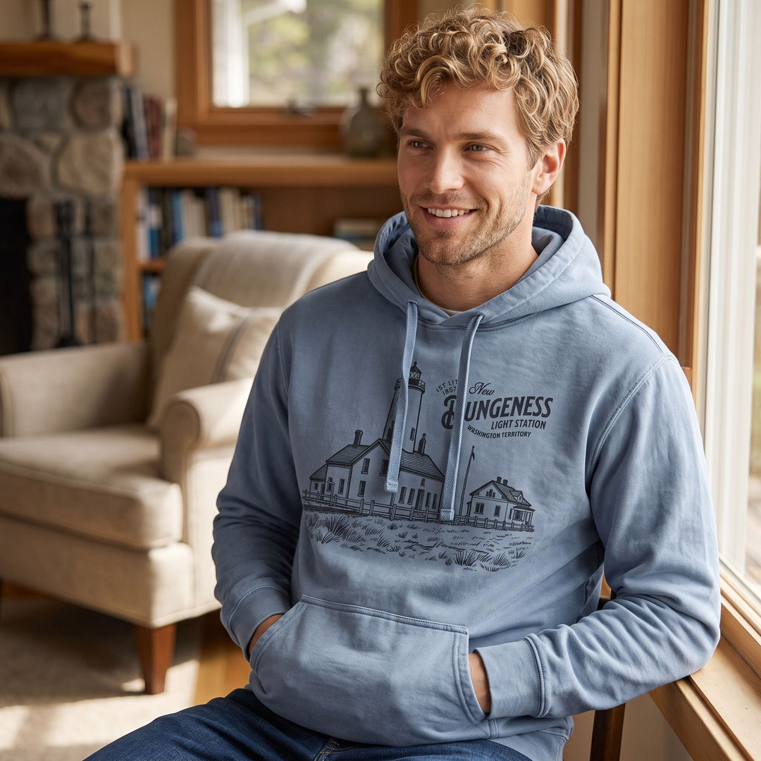 Comfortable man wearing the New Dungeness Light Station hoodie in a well-lit, cozy living space.