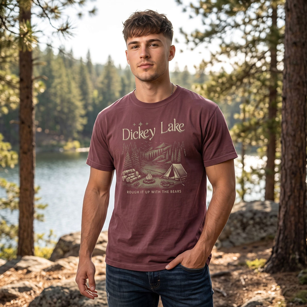 Casual young man wearing maroon garment-dyed heavyweight T-shirt outdoors amidst greenery and open sky.