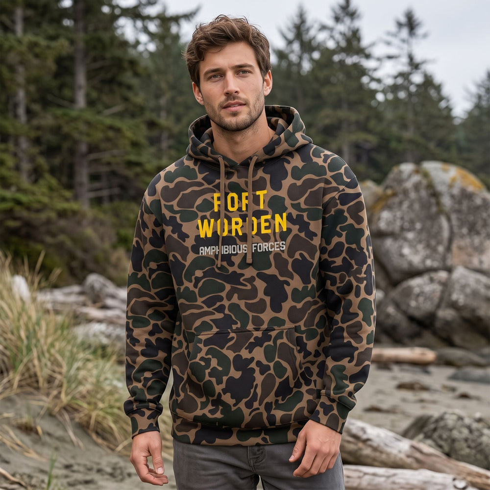 Adult model wearing the Fort Worden Amphibious Forces Hoodie in a natural outdoor setting with greenery, sunlight, and blurred foliage background.
