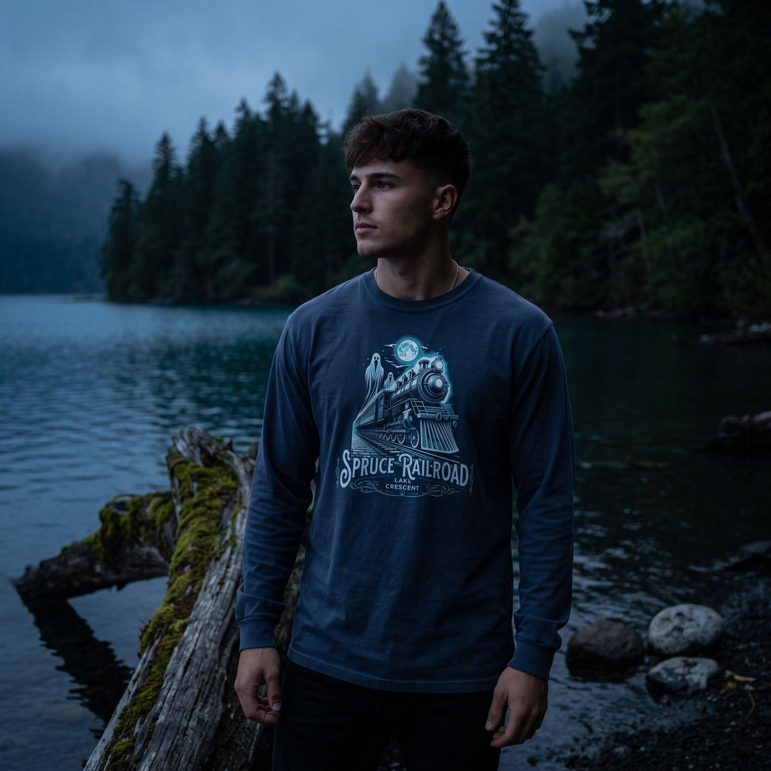 Casual young male model wearing vintage-inspired ghost train long sleeve shirt in a dark moody setting with deep shadows and rich textures.