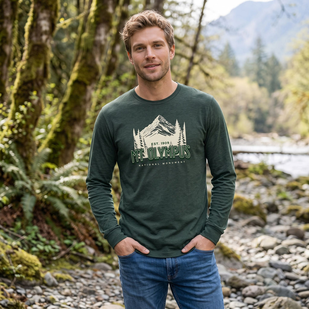 Polished male model wearing heritage-inspired long sleeve tee, outdoor setting with trees and rocks emphasizing rugged wilderness style