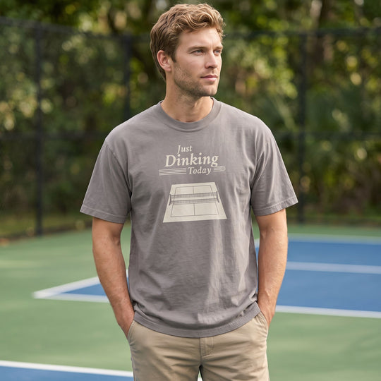 Adult model Ben wearing oversized pickleball t-shirt outdoors with natural greenery and bright sunlight, showcasing relaxed streetwear style.