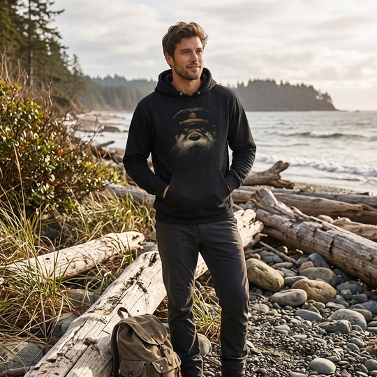 Adult model wearing The Kelp-Bed Boatswain hoodie outdoors with greenery and water, capturing a natural, casual lifestyle setting.