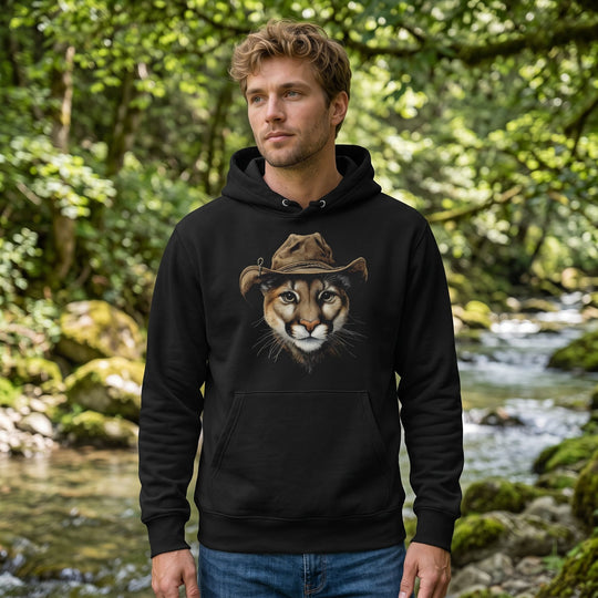 Male model wearing The Shadow Scout heavyweight hoodie in a natural outdoor setting with greenery and sunlight.
