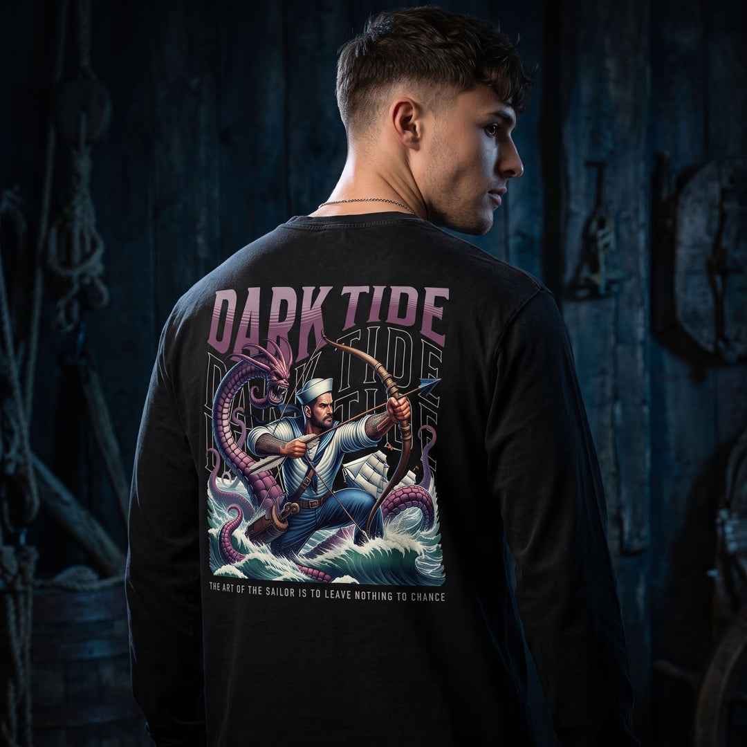 Casual styled young adult male model in a dark, moody setting showcasing a long sleeve shirt with sailor battling a sea serpent graphic, emphasizing maritime mythology.