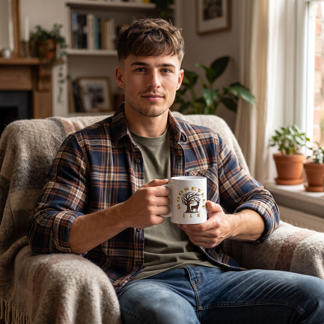 Young adult man enjoying tea or coffee from Theodore Roosevelt Elk Wilderness mug in a cozy, warm setting.