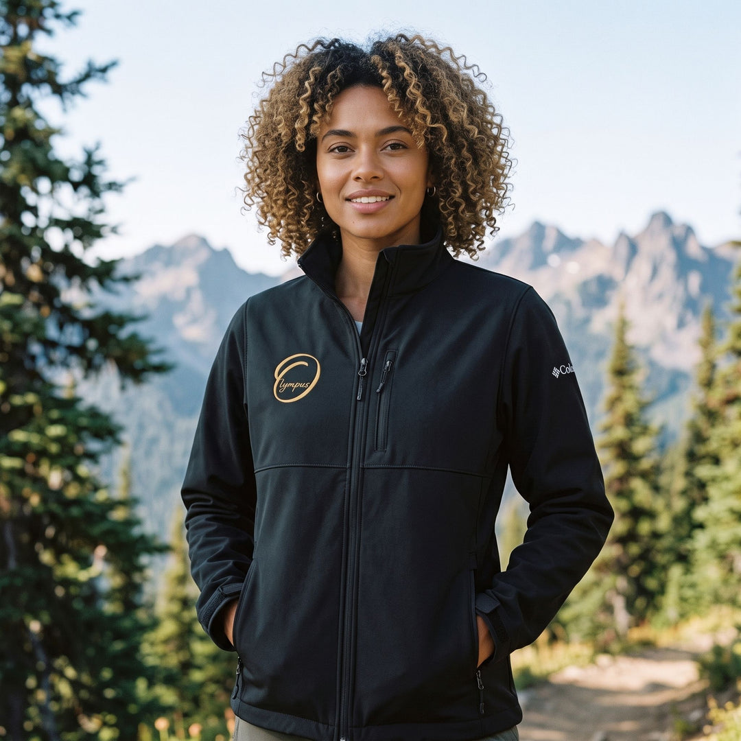 Outdoor scene with a model wearing the black Columbia soft shell jacket, surrounded by greenery and blue sky.