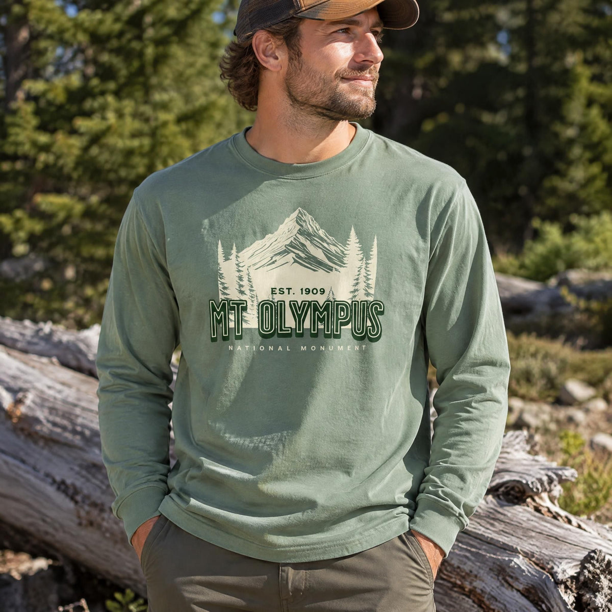 Person wearing a light green long sleeve shirt with a mountain graphic in a forest clearing.