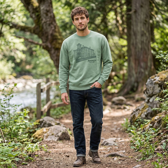 Outdoor scene featuring adult model in vintage-washed green sweatshirt with Admiralty Hall illustration near natural water and foliage