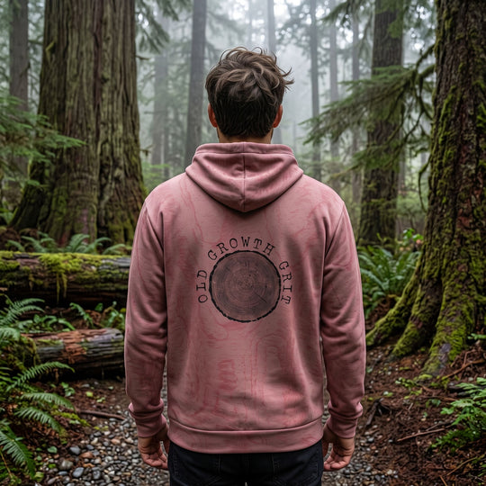 Casual man model wearing Old Growth Grit Hoodie outdoors in natural daylight with blurred foliage background.
