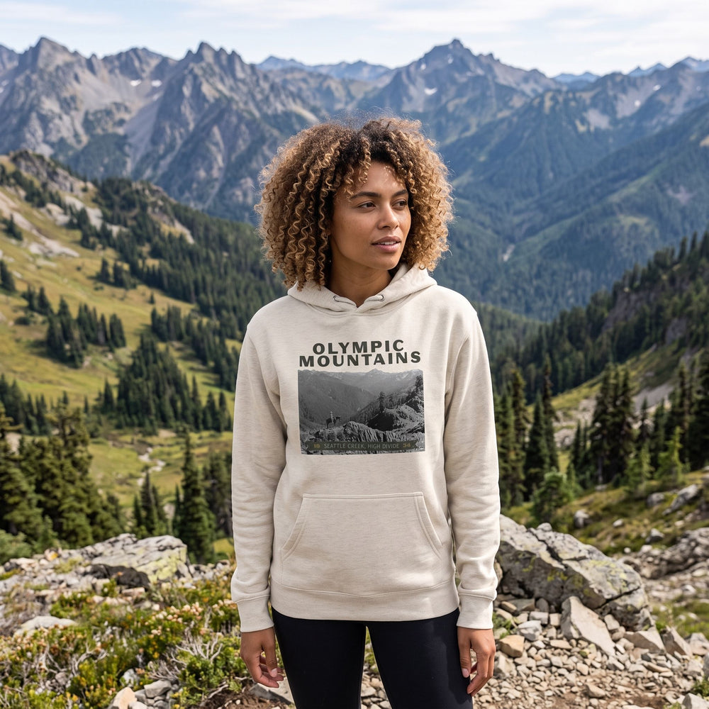Athletic woman model Zara wearing The Olympic Mountains 'High Divide' heavyweight hoodie in outdoor setting with greenery, natural daylight.
