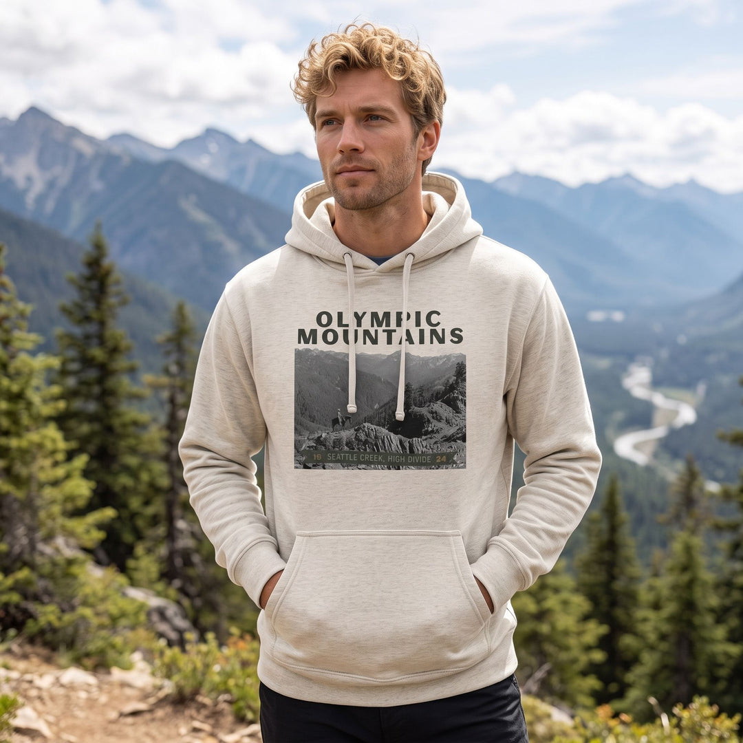 Adult model wearing The Olympic Mountains High Divide Heavyweight Hoodie outdoors with greenery in the background, bright natural light, showcasing the product&