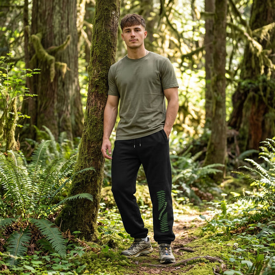 Young adult model wearing Bushwacker Sword Fern sweatpants in lush outdoor landscape, highlighting botanical print and relaxed outdoor look.
