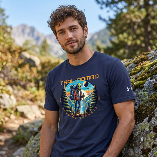 Model sporting alien hiker T-shirt in outdoor setting with mountain and sky backdrop, natural light highlighting the design.