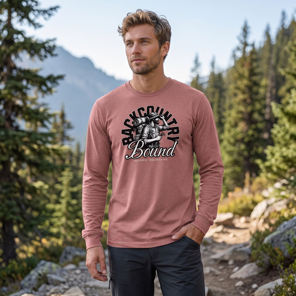Adult male model wearing The Backcountry Bound Long Sleeve Tee in outdoor setting with greenery, rocks, blurred foliage, emphasizing rugged, nature-inspired style.