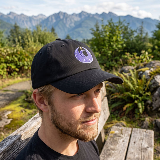 Casual person wearing Falcon Sky-Breaker baseball hat with embroidered design outdoors, sitting on a rustic wooden bench amid lush foliage on a sunny day.