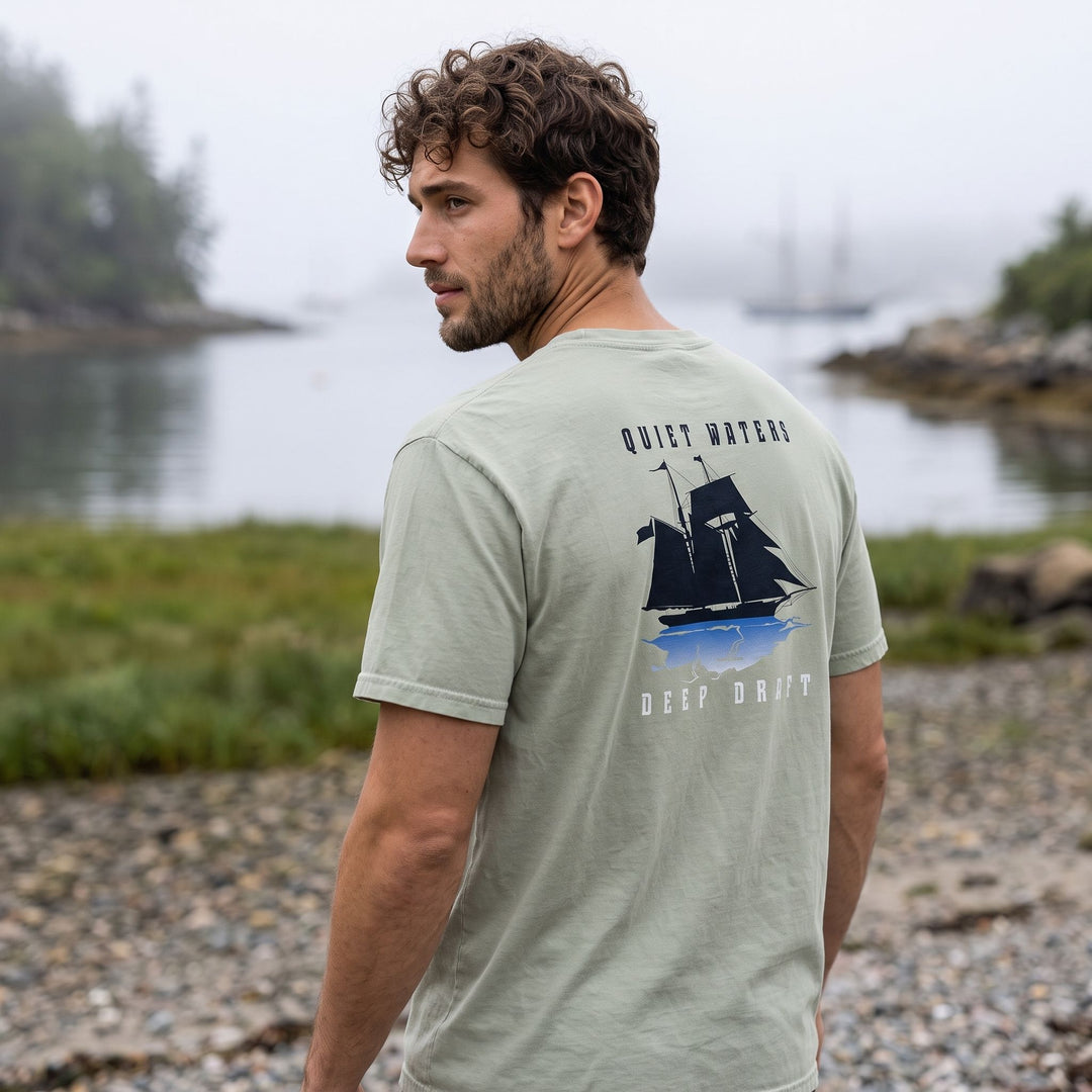 Casual outdoor scene with model Alex wearing a deep draft quiet waters heavyweight garment-dyed t-shirt among greenery and water, showcasing relaxed style.