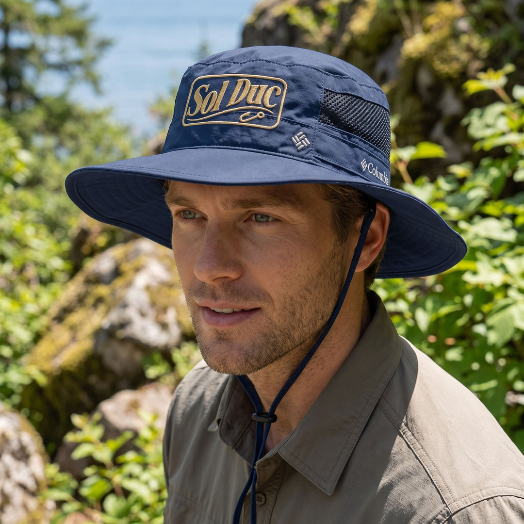 Adult male wearing Sol Duc Booney Hat in outdoor setting with greenery and sky, demonstrating sun shade and moisture-wicking features