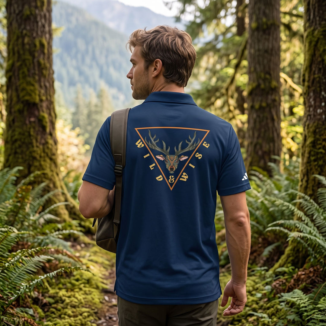 The back of a collegiate navy adidas sport polo showing a mystical elk head gold linework graphic in an outdoor setting.