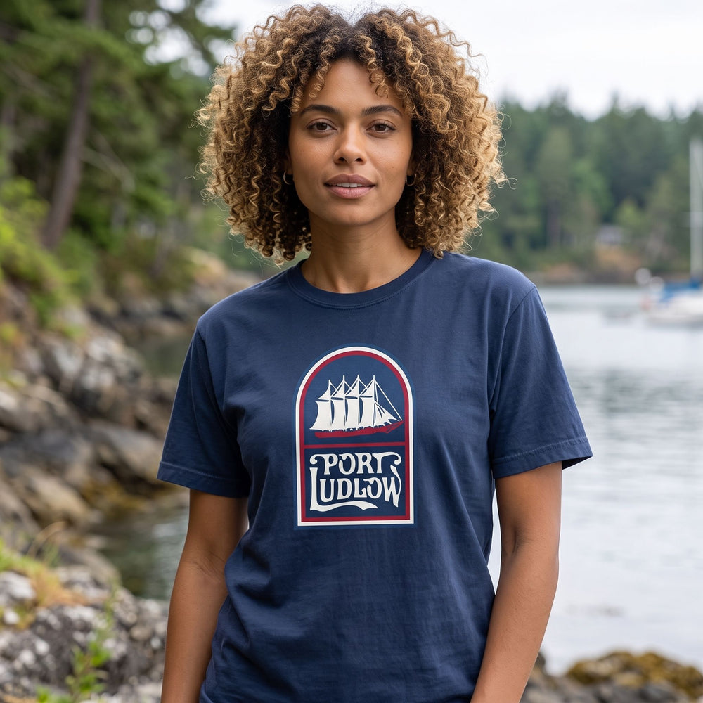 Model wearing Port Ludlow 1968 heavyweight tee outdoors with greenery, natural daylight, and blurred foliage background