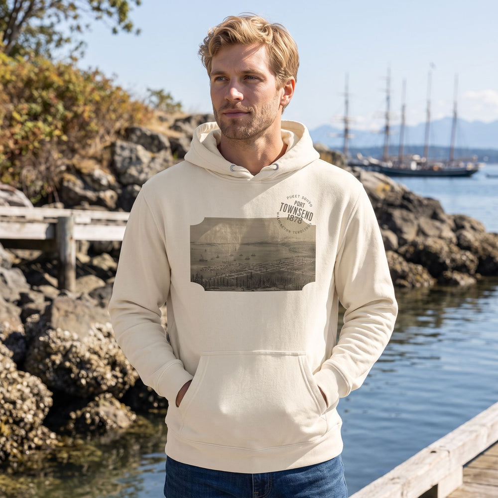Adult model wearing Port Townsend 1878 Heavyweight Hoodie outdoors in natural daylight, surrounded by greenery, rocks, and water, showcasing casual style.