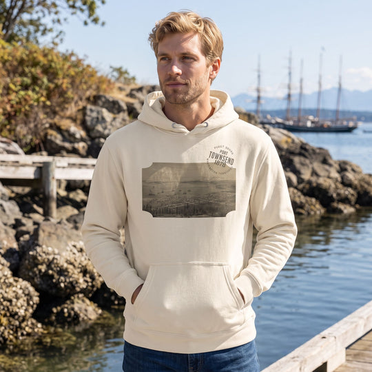 Adult model wearing Port Townsend 1878 Heavyweight Hoodie outdoors in natural daylight, surrounded by greenery, rocks, and water, showcasing casual style.