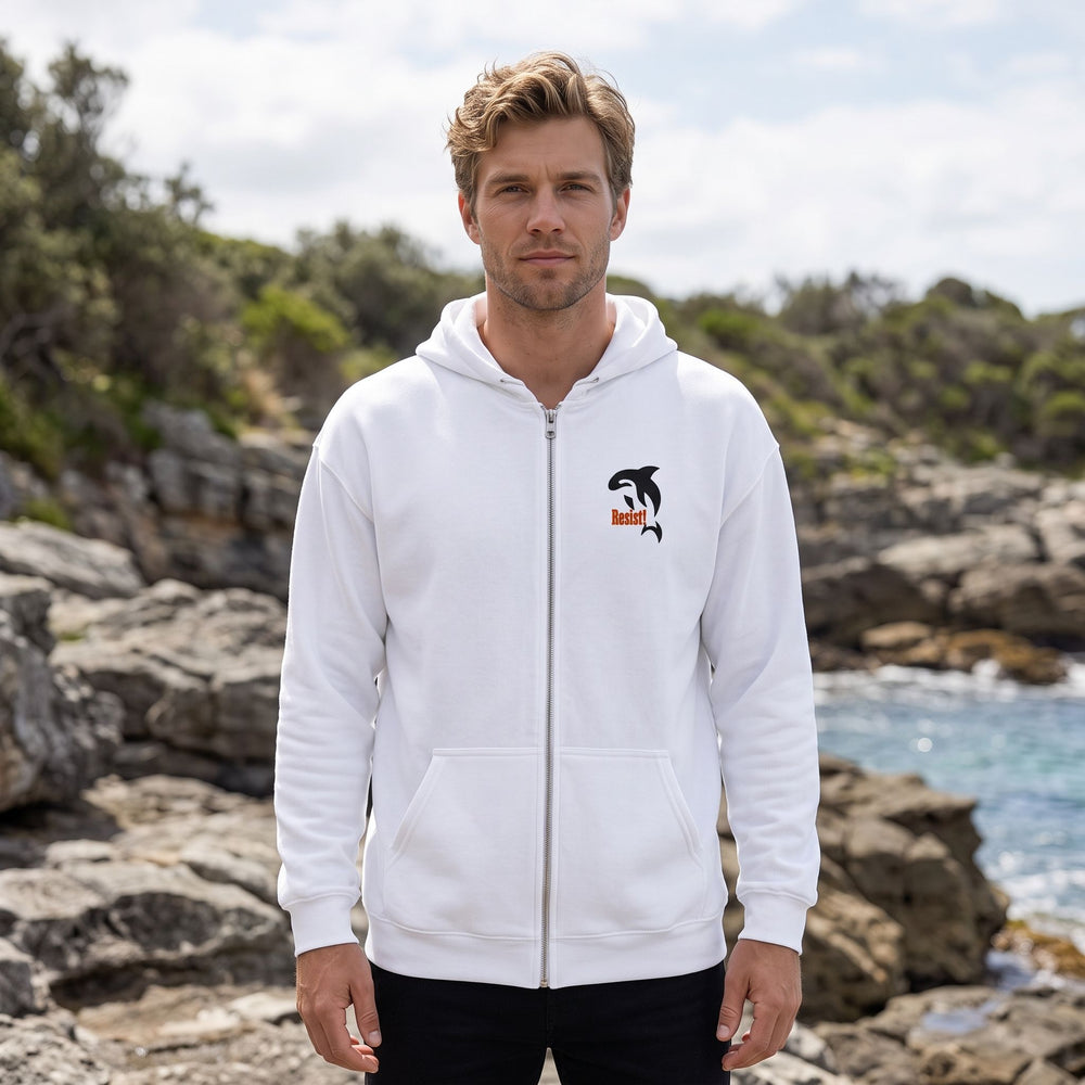 Adult model wearing Resist! embroidered orca fleece zip-up in an outdoor setting with greenery, under bright sunlight, demonstrating a casual style.