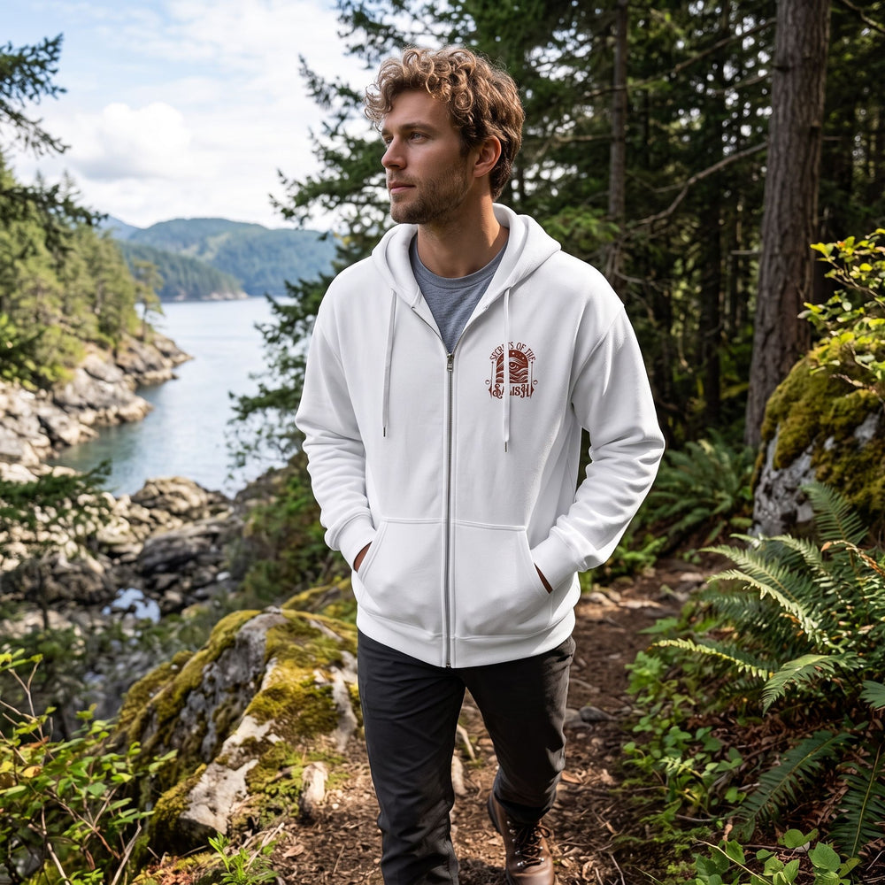 Adult model wearing Salish Eye Full-Zip Hoodie outdoors with greenery and water in the background, showcasing a casual, rugged appearance suitable for coastal weather.