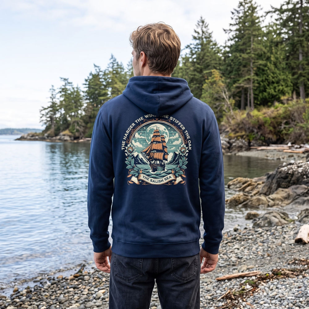 Man wearing The Iron Oak Salish Sea Hoodie in a natural outdoor setting with greenery and water, highlighting the hoodie’s relaxed fit and design.