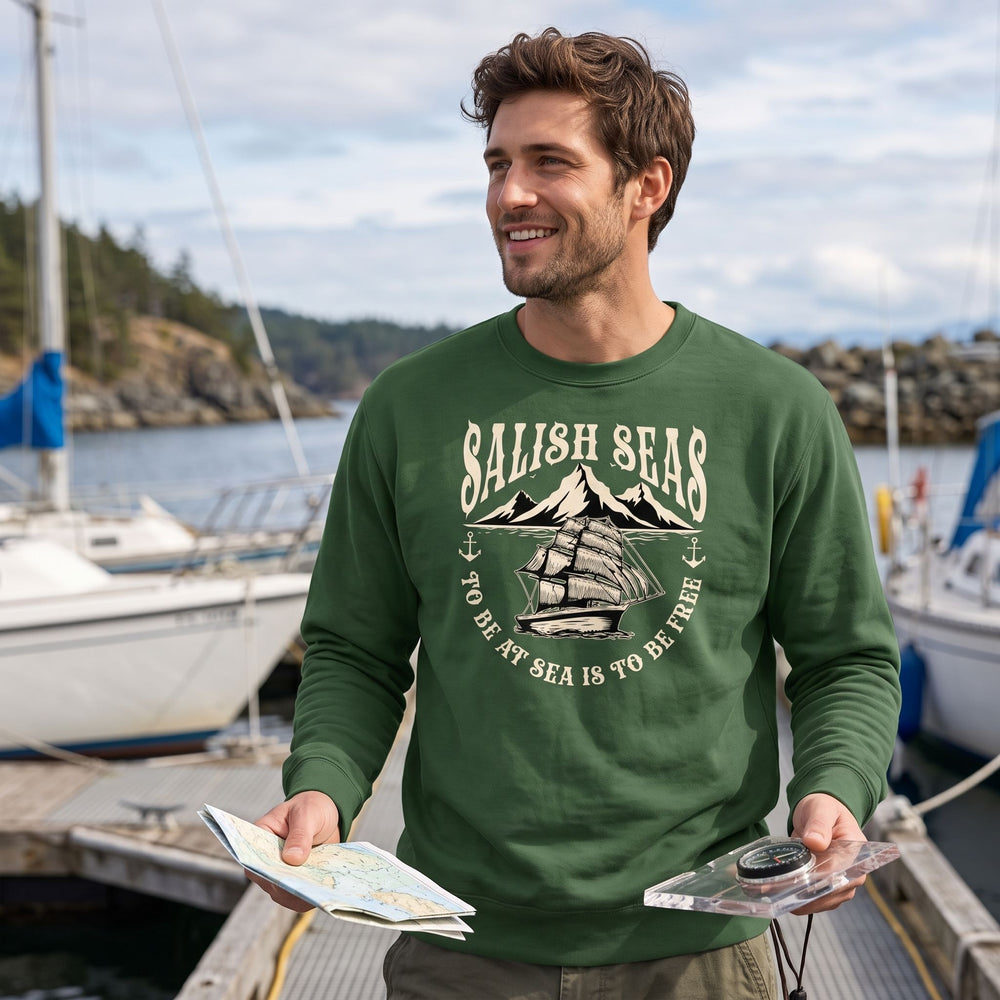 Men's Salish Seas sweatshirt featuring sailing ship graphic in outdoor natural setting with greenery and water, casual style by model Alex.