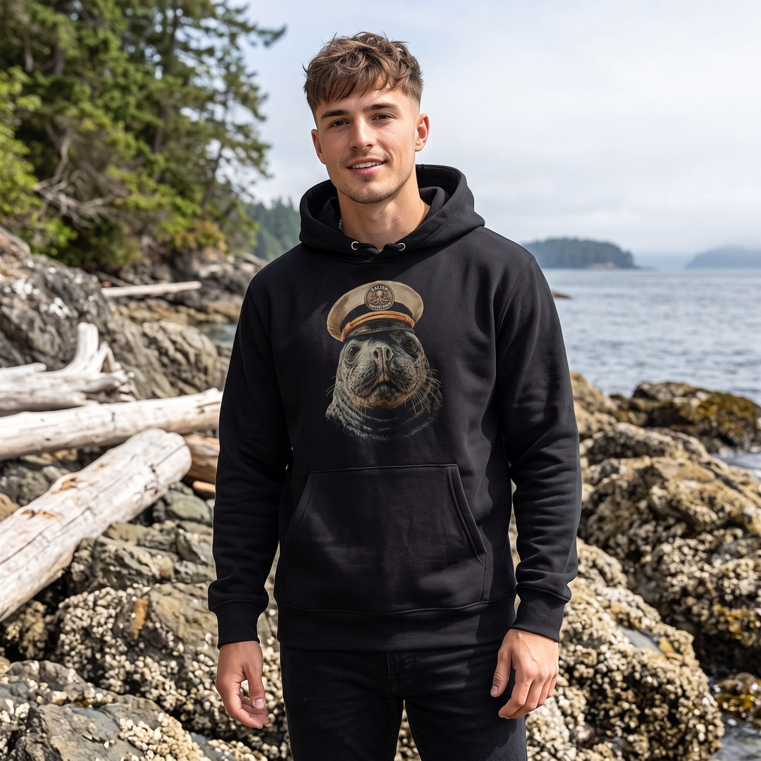 Young adult model wearing the Salty Skipper heavyweight hoodie outdoors with greenery and water in the background, capturing a natural and fresh scene.