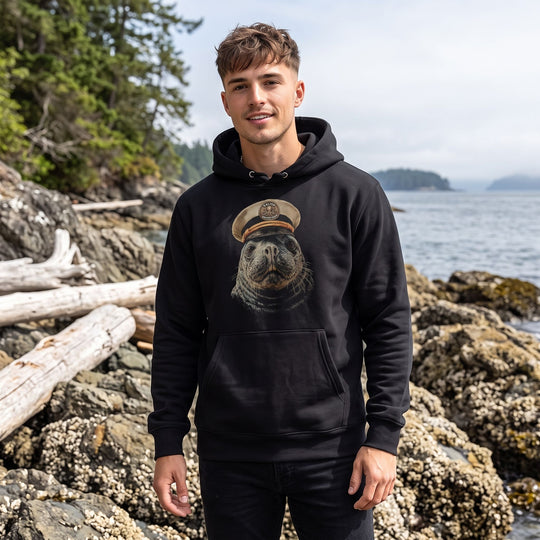 Young adult model wearing the Salty Skipper heavyweight hoodie outdoors with greenery and water in the background, capturing a natural and fresh scene.