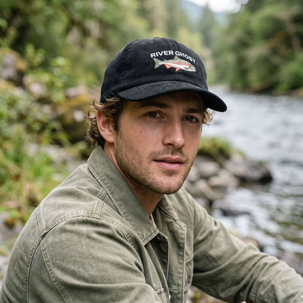 A man wearing the Steelhead Run cotton corduroy cap while standing by a riverbank in natural outdoor daylight.