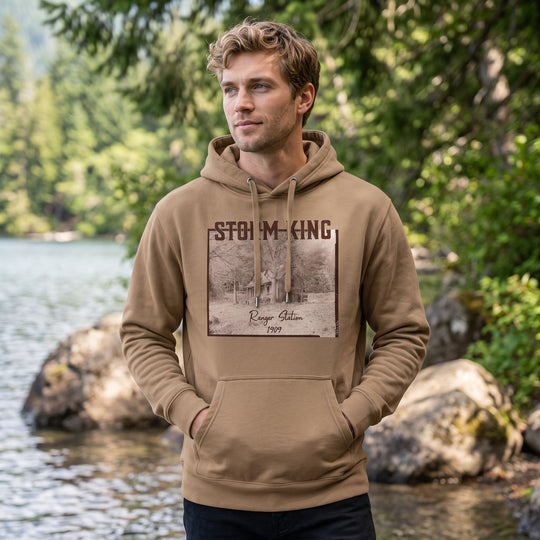 Adult model Ben wearing the Storm King Ranger Station heavyweight hoodie in outdoor setting with greenery and bright sunlight.