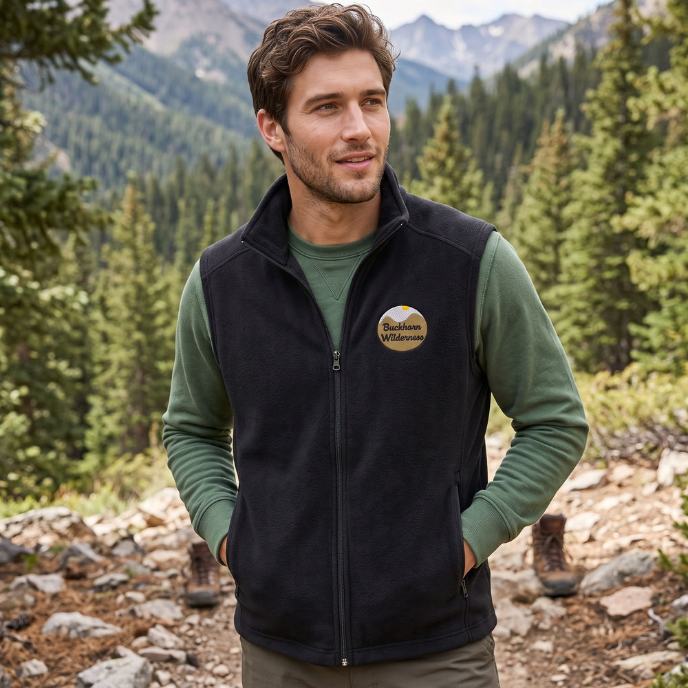 Outdoor scene featuring a model wearing The Buckhorn High-Country Vest in natural daylight with lush greenery, highlighting its suitability for hiking and outdoor activities in rugged terrain.
