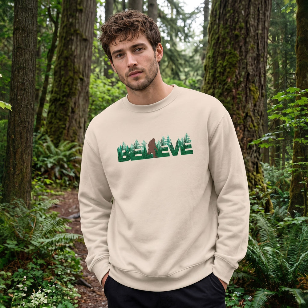 Casual model wearing the oversized fleece in a lush outdoor setting with greenery, rocks, and blurred foliage, showcasing the Sasquatch graphic.