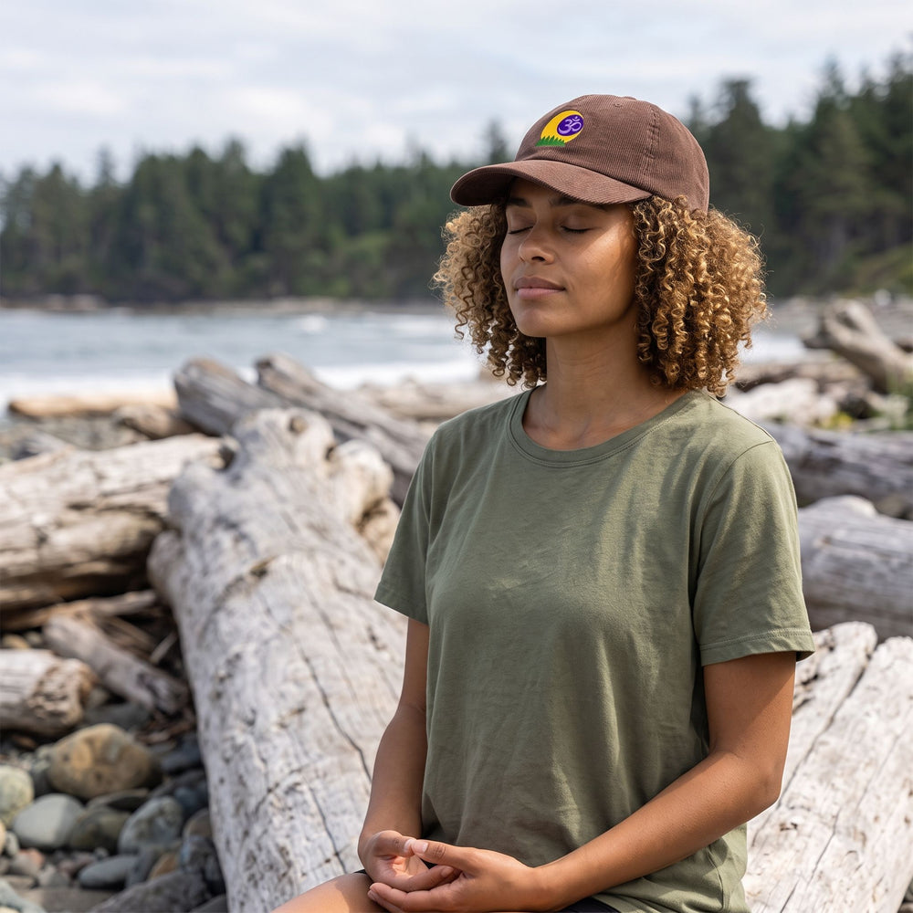 Outdoor scene featuring a model wearing the Forest Om Corduroy Meditation Cap in a natural setting with greenery, showcasing relaxed style and connection to nature.