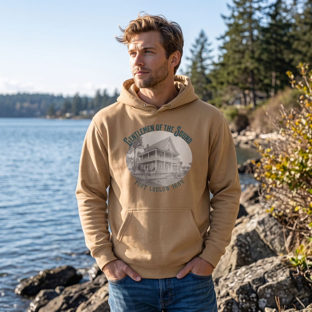 Adult male model wearing The Gentlemen of the Sound Heavyweight Hoodie in an outdoor setting with greenery, bright sunlight, and a blurred nature background.