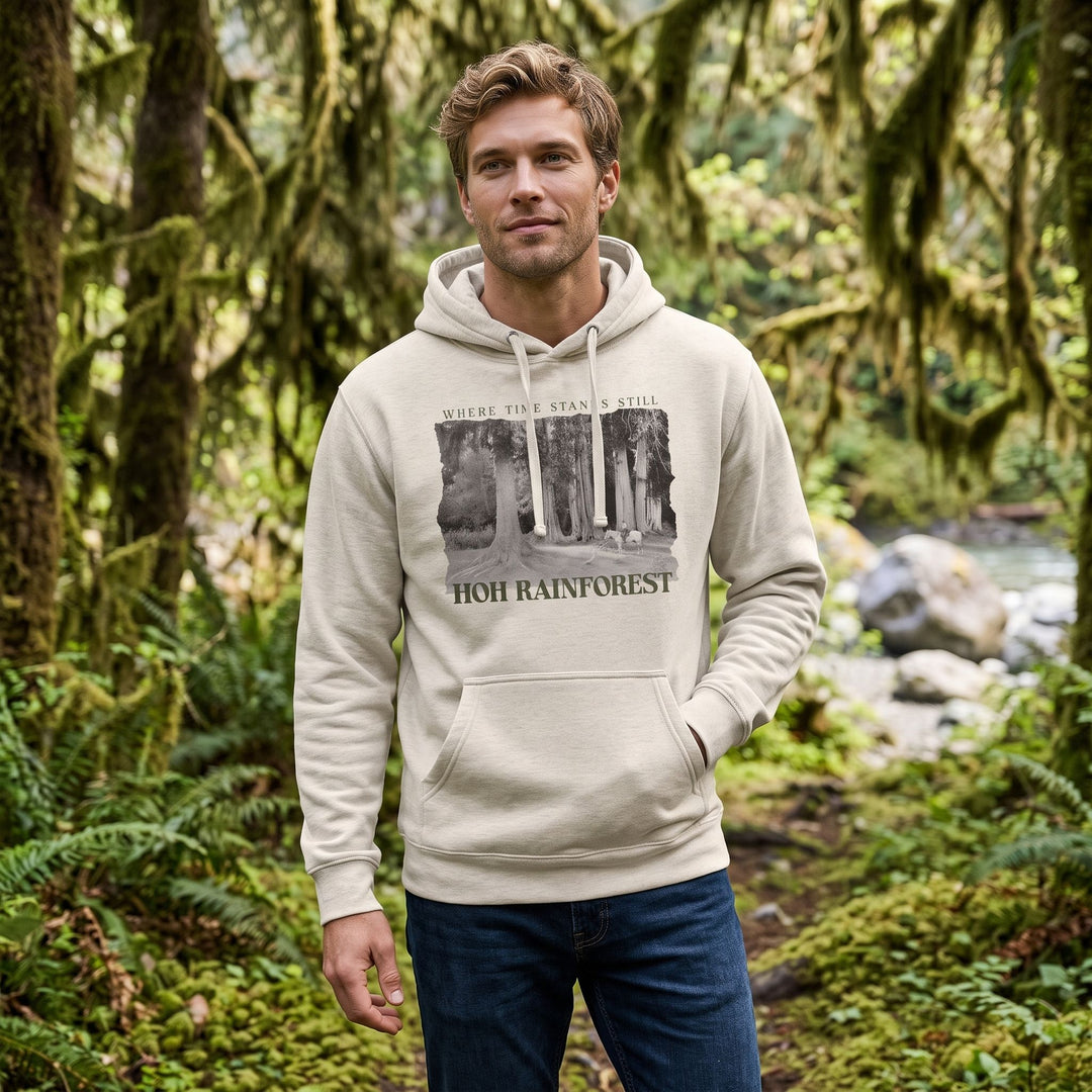 Adult male model wearing The Hoh Rainforest heavyweight hoodie outdoors with natural sunlight, surrounded by greenery and blurred foliage