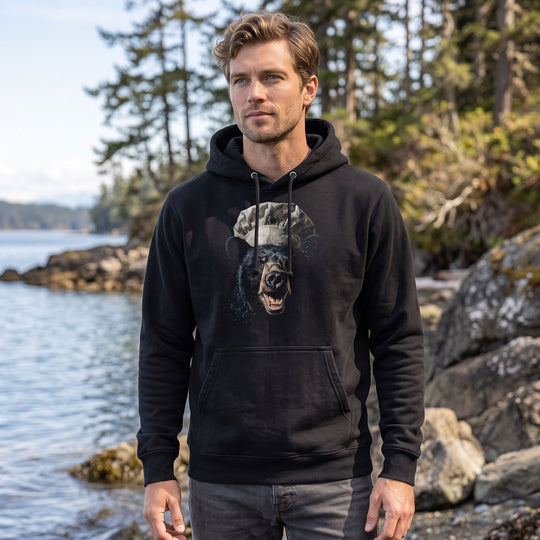 Black Bear wearing The Mess Officer heavyweight hoodie outdoors, surrounded by greenery and natural elements, under bright sunlight.