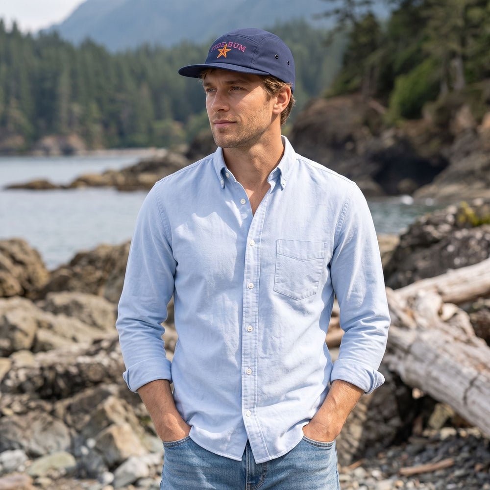 Adult model wearing the Tide Bum Camper Cap outdoors with greenery and water in the background, showcasing coastal comfort and style.