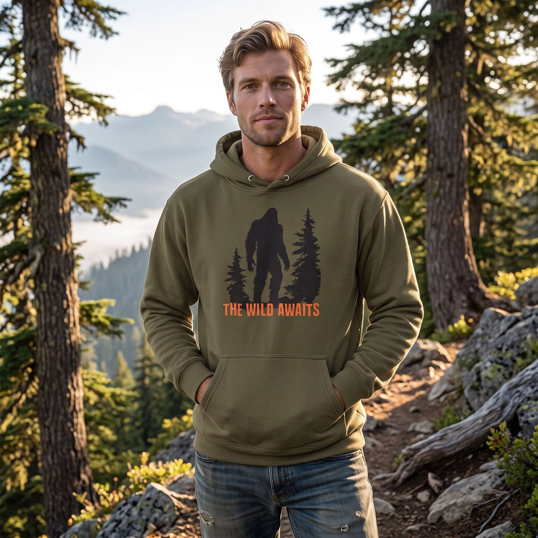 Outdoor scene featuring the Wild Awaits Hoodie with Sasquatch silhouette on a model in natural daylight, surrounded by greenery and rocks.