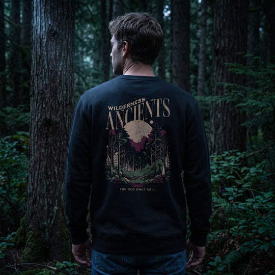 Male model wearing Wilderness Ancients Crewneck in a dark moody setting with deep shadows and rich textures.